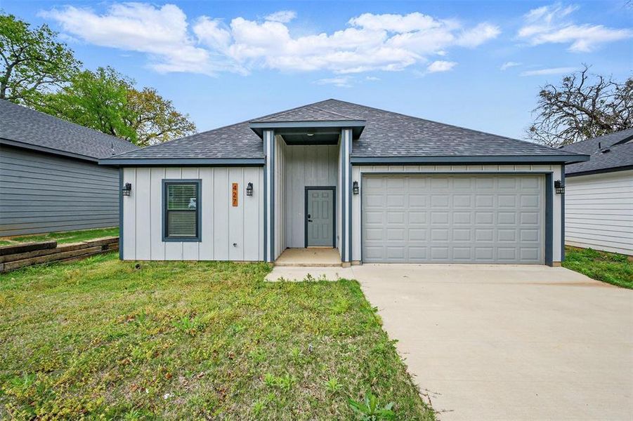 View of front of house with board and batten siding, roof with shingles, a front yard, an attached garage, and concrete driveway