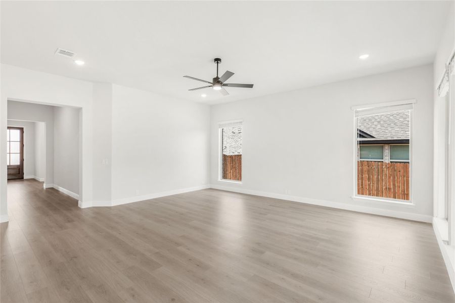 Open living room with light wood floors, ceiling fan, and two windows Open living room with light wood floors, ceiling fan, and two windows