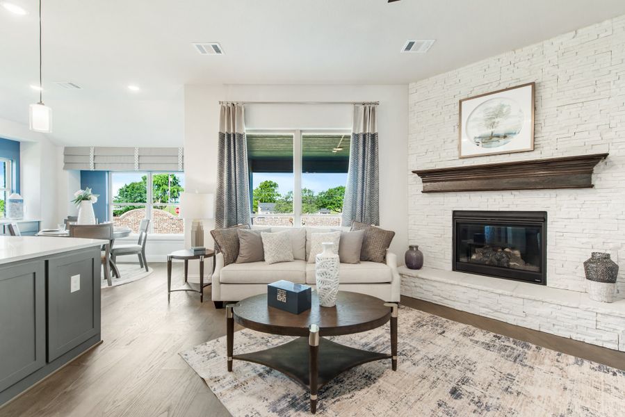 Open-concept living room with white stone fireplace, beige sofa, and hardwood floors open to dining area