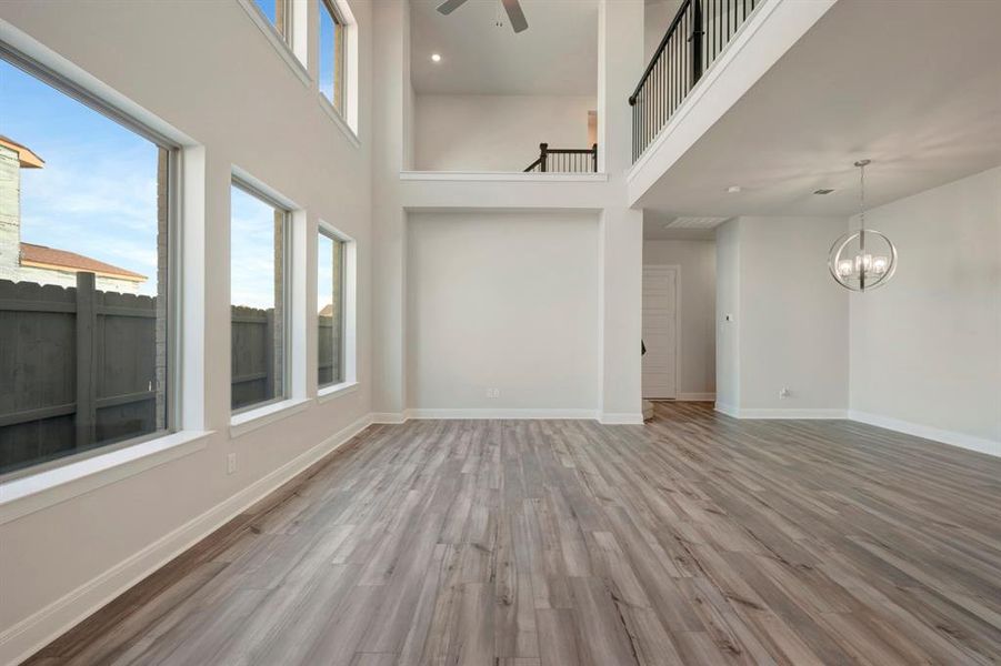 Unfurnished living room featuring a high ceiling, light wood finished floors, ceiling fan, and hanging lights