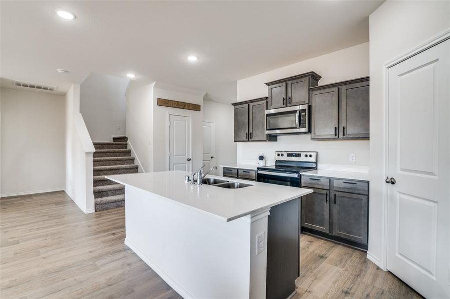 Kitchen with stainless steel appliances, light wood finished floors, an island with sink, dark wood finish cabinetry, and recessed lighting Kitchen with stainless steel appliances, light wood finished floors, an island with sink, dark wood finish cabinetry, and recessed lighting
