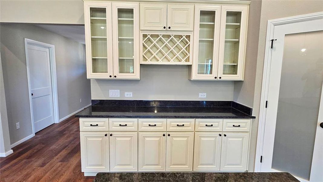 Kitchen with dark wood-style flooring, glass insert cabinets, and dark stone counters