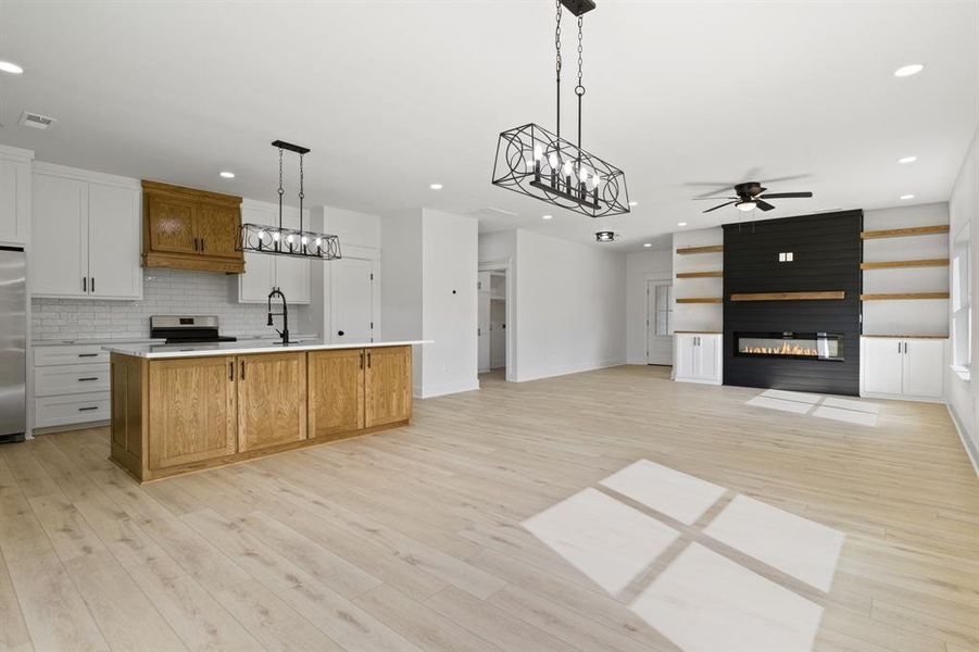 Kitchen with brown cabinetry, white cabinets, hanging light fixtures, a chandelier, and a center island with sink