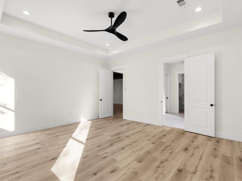 Unfurnished bedroom featuring a raised ceiling, light wood-style flooring, a ceiling fan, and recessed lighting