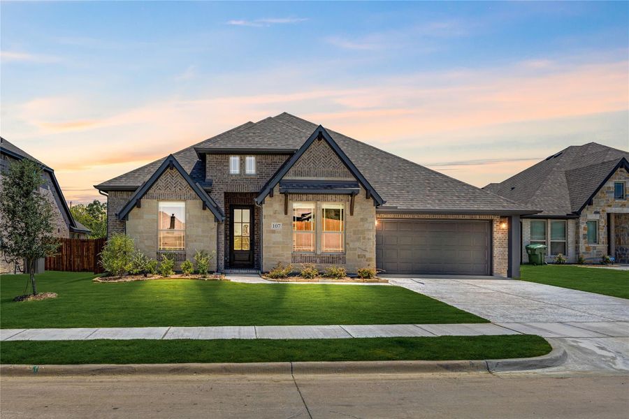 Single-story home with brick and stone exterior, two-car garage, and manicured front lawn at dusk Single-story home with brick and stone exterior, two-car garage, and manicured front lawn at dusk