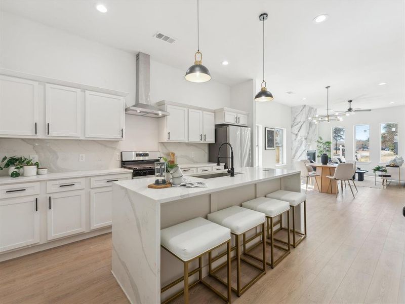 Kitchen with visible vents, wall chimney range hood, appliances with stainless steel finishes, an island with sink, and decorative light fixtures