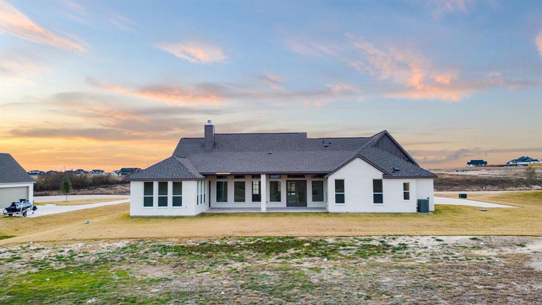 Back house at dusk with a lawn and central air condition unit