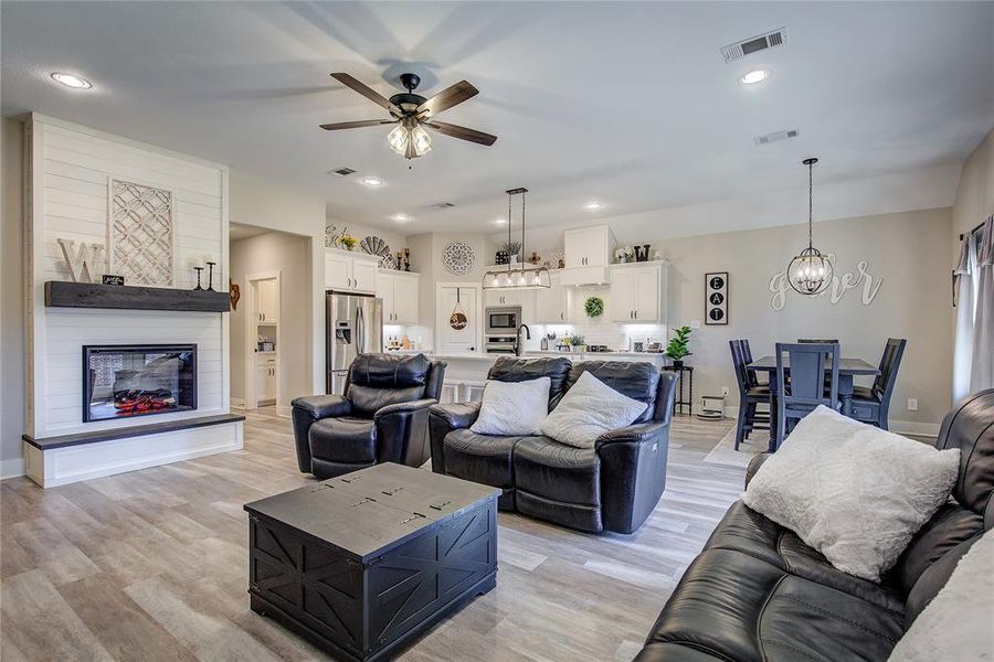 Living room with a large fireplace, light hardwood / wood-style flooring, ceiling fan with notable chandelier, and sink