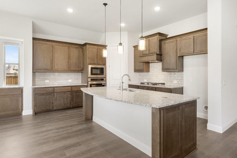 Kitchen with brown wood cabinets, granite island with sink, pendant lights, and stainless steel appliances Kitchen with brown wood cabinets, granite island with sink, pendant lights, and stainless steel appliances