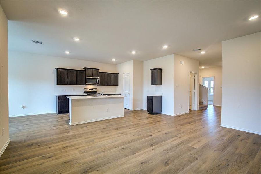 Kitchen with an island with sink, open floor plan, light wood-type flooring, appliances with stainless steel finishes, and recessed lighting