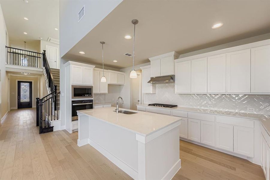 Kitchen featuring tasteful backsplash, pendant lighting, white cabinets, an island with sink, and light wood-style floors
