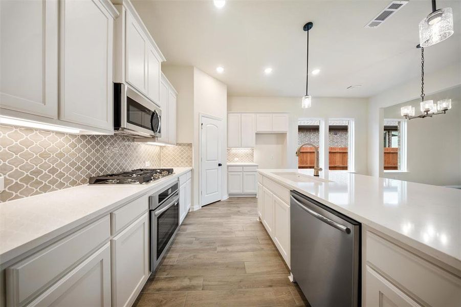 Kitchen with appliances with stainless steel finishes, light wood finished floors, white cabinets, decorative backsplash, and recessed lighting