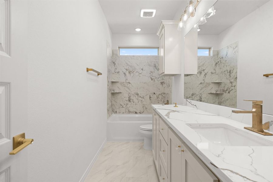 Bathroom featuring double vanity, washtub / shower combination, and light marble finish floors