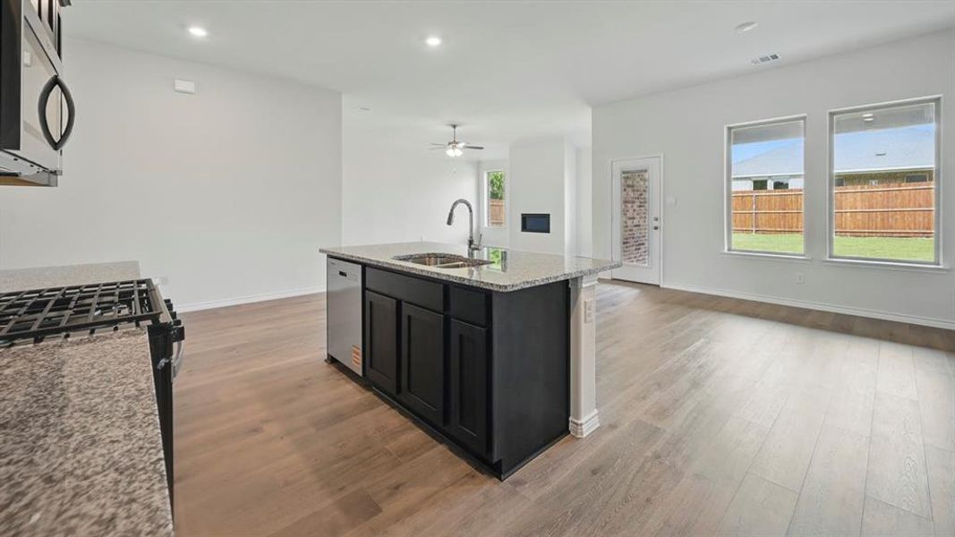 Kitchen with light stone counters, stainless steel appliances, an island with sink, recessed lighting, and open floor plan