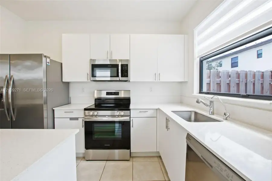 Kitchen featuring white cabinetry, solid-surface countertops, stainless steel appliances, ceramic tile flooring, and a large horizontal window