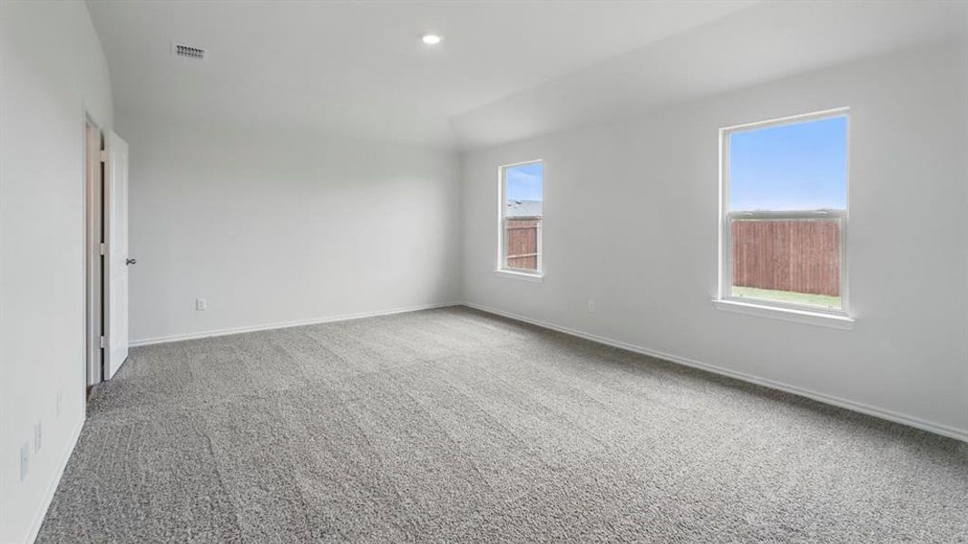 Spacious room with grey textured carpeting, two rectangular windows, vaulted ceiling, and recessed lighting