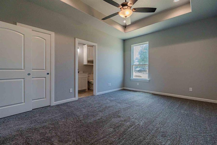 Unfurnished bedroom with a raised ceiling, carpet flooring, ensuite bathroom, and a ceiling fan Unfurnished bedroom with a raised ceiling, carpet flooring, ensuite bathroom, and a ceiling fan