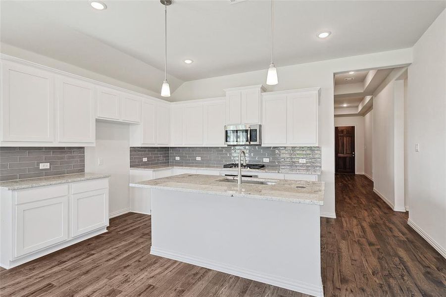 Kitchen with pendant lighting, a kitchen island with sink, white cabinetry, dark hardwood / wood-style flooring, and decorative backsplash