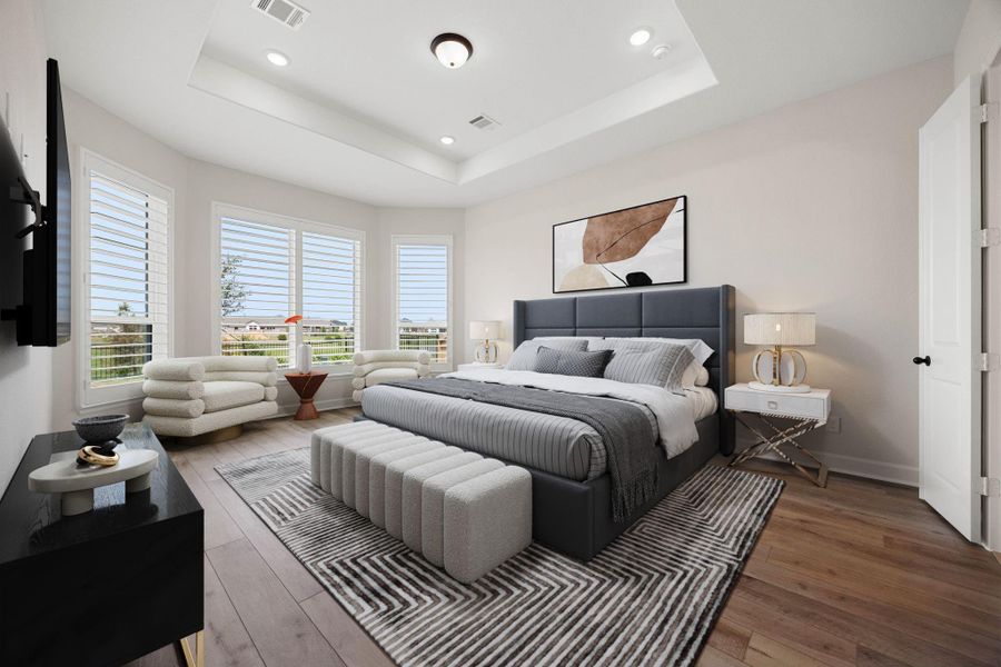 Luxurious primary bedroom retreat offering a peaceful sanctuary on the main level. This expansive suite features a dramatic tray ceiling accented by elegant recessed lighting, wide-plank wood-look flooring, and a generous layout. A beautiful bay window seating area is equipped with custom plantation shutters, framing stunning views of the green backyard and community lake while bathing the room in natural light. *Virtually Staged Luxurious primary bedroom retreat offering a peaceful sanctuary on the main level. This expansive suite features a dramatic tray ceiling accented by elegant recessed lighting, wide-plank wood-look flooring, and a generous layout. A beautiful bay window seating area is equipped with custom plantation shutters, framing stunning views of the green backyard and community lake while bathing the room in natural light. *Virtually Staged