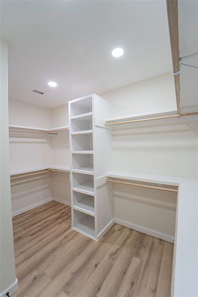 Large Custom Walk-in closet accommodates the primary bedroom, featuring built-in shelving, hanging rods, recessed lighting, and wood-finish flooring
