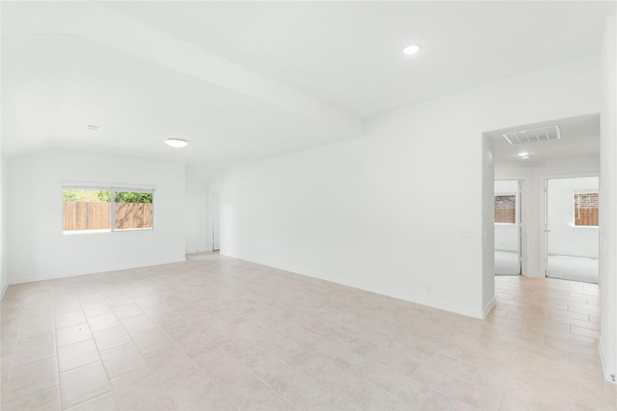 Empty living room with white walls, tile floors, vaulted ceiling, and doorway to adjacent room