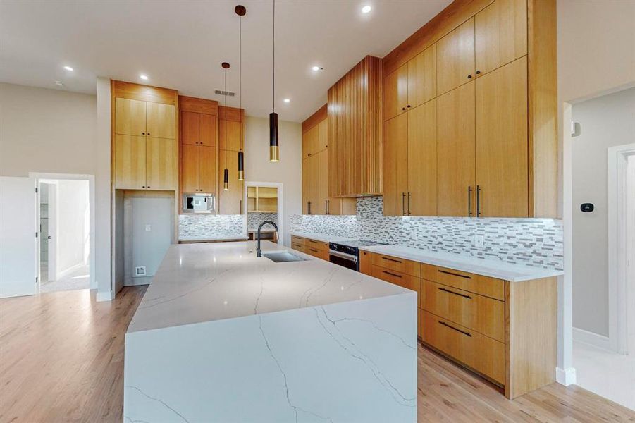 Kitchen featuring a large island with sink, sink, electric range, light hardwood / wood-style floors, and light stone counters