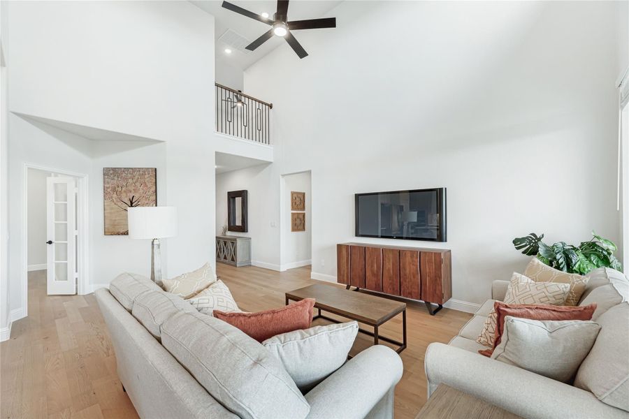Living room with two-story ceiling, ceiling fan, hardwood floors, and wall-mounted TV above wood console