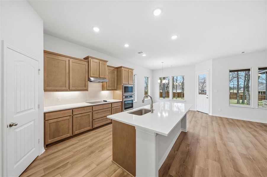 Kitchen featuring wood finish cabinetry, a kitchen island with sink, suspended lighting, and light wood-style flooring Kitchen featuring wood finish cabinetry, a kitchen island with sink, suspended lighting, and light wood-style flooring