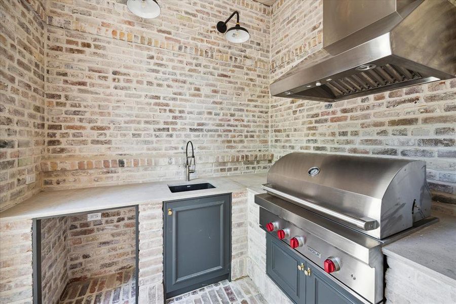 The outdoor kitchen features a built-in stainless steel Wolf grill and vent hood, an under-mount sink, and space for a beverage refrigerator.