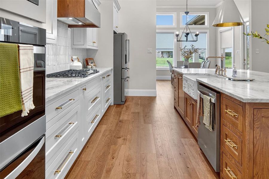 Kitchen with light stone counters, white cabinetry, light wood-style floors, decorative light fixtures, and brown cabinetry