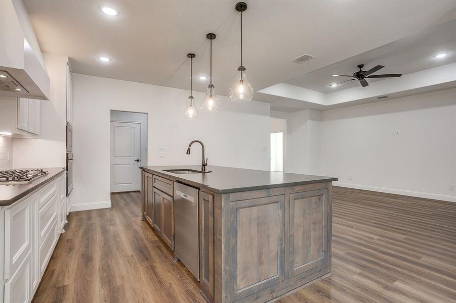 Kitchen with a center island with sink, pendant lighting, exhaust hood, white cabinetry, and a ceiling fan