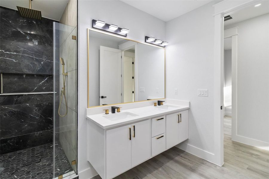 Bathroom with double vanity, a marble finish shower, and light wood-style floors
