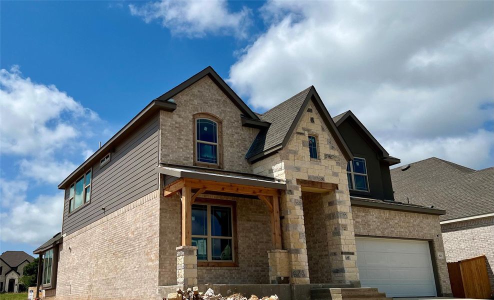View of front facade featuring a garage, brick siding, stone siding, roof with shingles, and driveway View of front facade featuring a garage, brick siding, stone siding, roof with shingles, and driveway