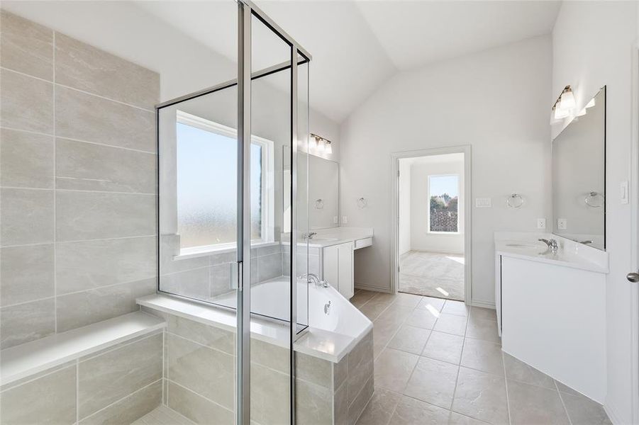 Full bath with vaulted ceiling, a bath, two vanities, a shower stall, and light tile patterned floors
