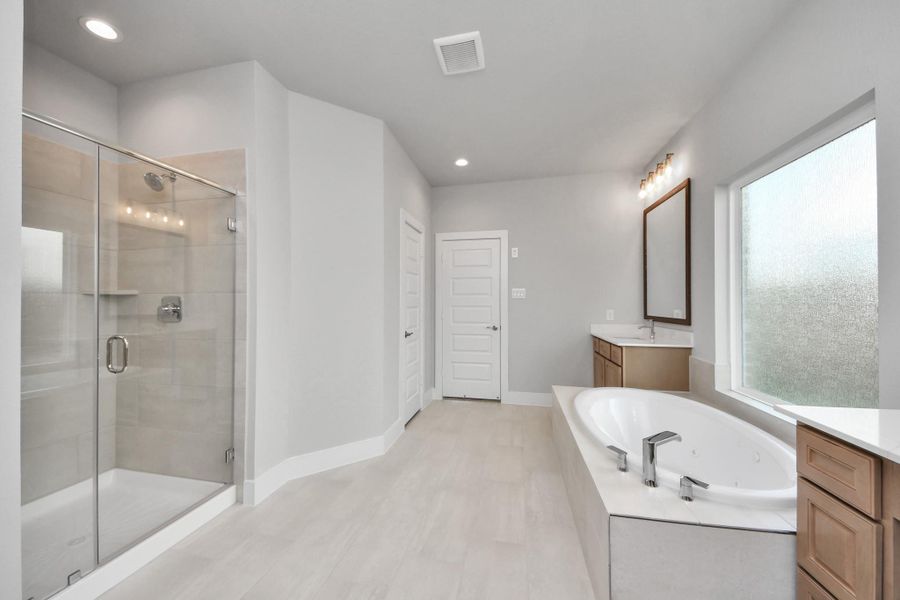 Escape to a spa-like oasis in this primary bathroom. Enjoy a walk-in shower with tile surround, a separate garden tub with custom detailing, and an elegant vanity featuring light countertops, modern hardware, and beautiful vanity lights. Experience luxury and relaxation in every detail.