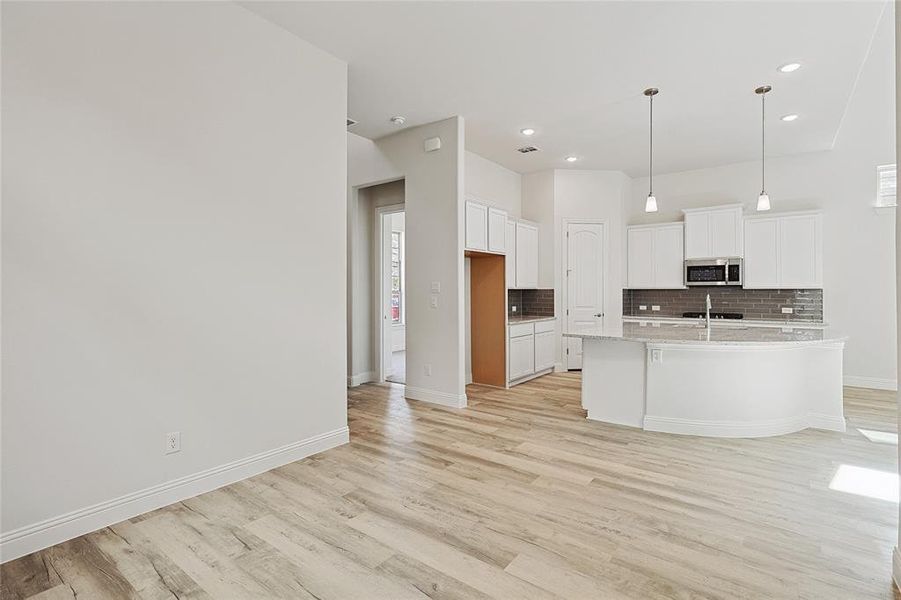 Kitchen with hanging light fixtures, light hardwood / wood-style flooring, decorative backsplash, a center island with sink, and white cabinets