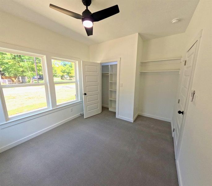 Unfurnished bedroom with dark carpet, a ceiling fan, and a spacious closet Unfurnished bedroom with dark carpet, a ceiling fan, and a spacious closet
