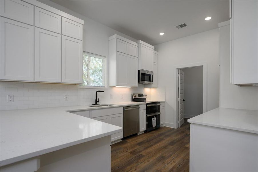 Kitchen with sink, appliances with stainless steel finishes, white cabinets, dark wood-type flooring, and decorative backsplash