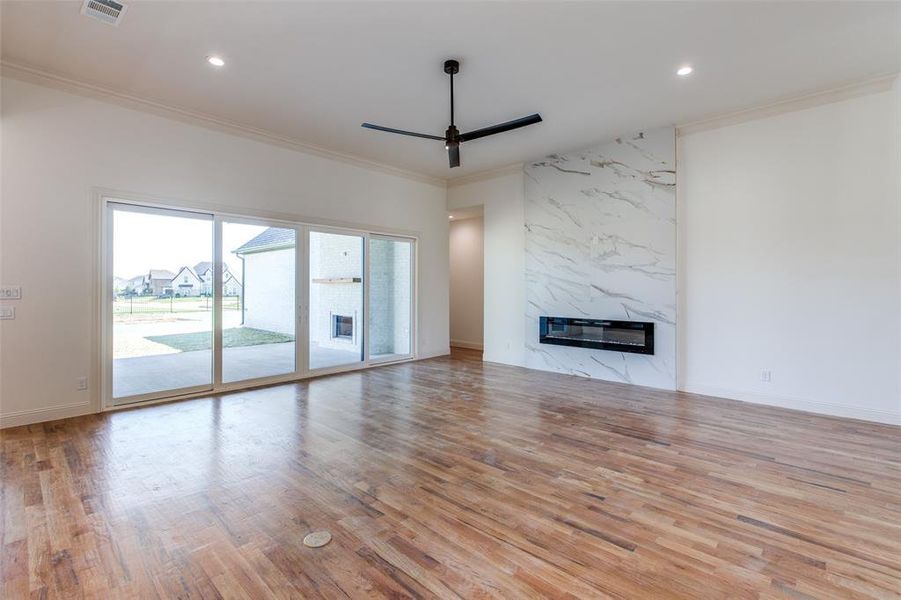 Unfurnished living room with light wood-type flooring, ornamental molding, ceiling fan, and a high end fireplace