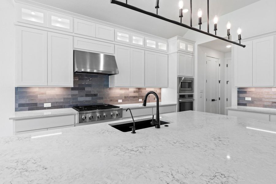 Kitchen with light stone counters, decorative backsplash, wall chimney range hood, and white cabinets