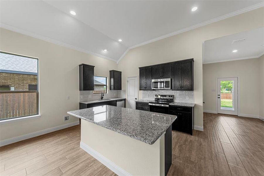 Kitchen with a central island featuring a granite countertop, dark wood-finish cabinetry, stainless steel appliances, and a tile backsplash