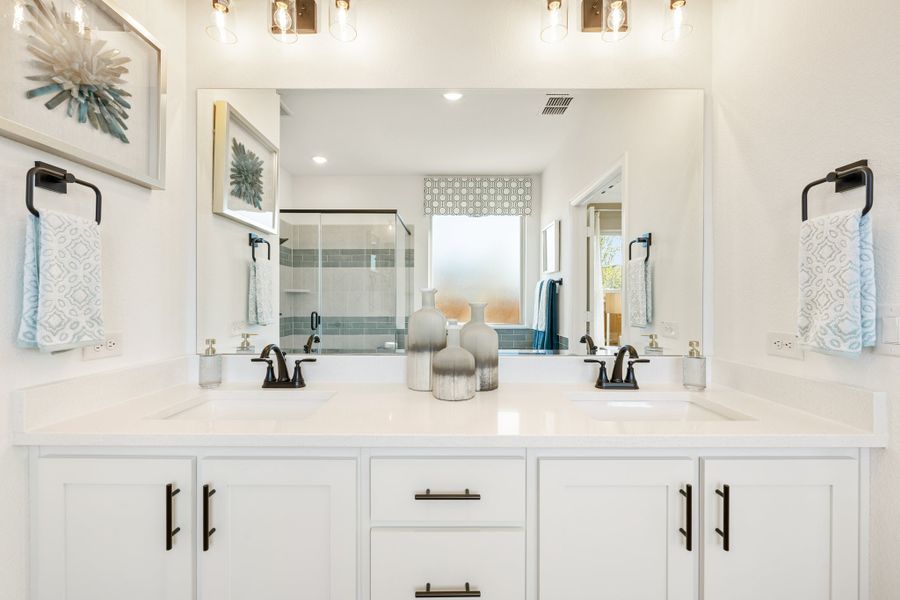 Master bathroom with double vanity, white cabinets, large mirror, and glass shower in background
