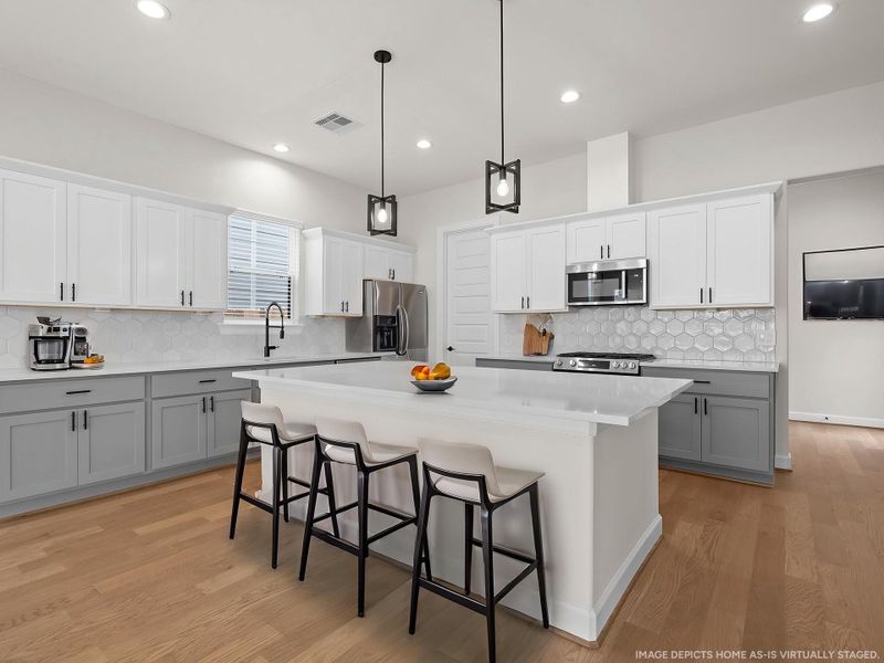 The chef-inspired kitchen featuring sleek finishes, smart storage, and a seamless flow into the main living areas. Image depicts home as-is virtually staged.