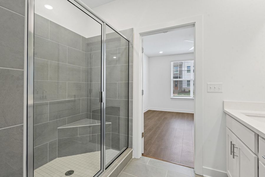 Walk-in shower with gray tile surround, integrated corner bench, and glass enclosure