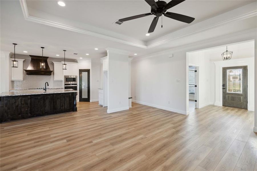 Unfurnished living room featuring light hardwood / wood-style flooring, ceiling fan with notable chandelier, and a tray ceiling