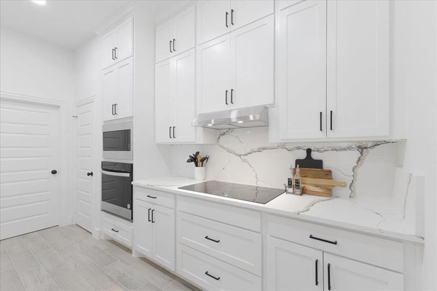 Kitchen with white cabinetry, light stone countertops, oven, under cabinet range hood, and black electric cooktop