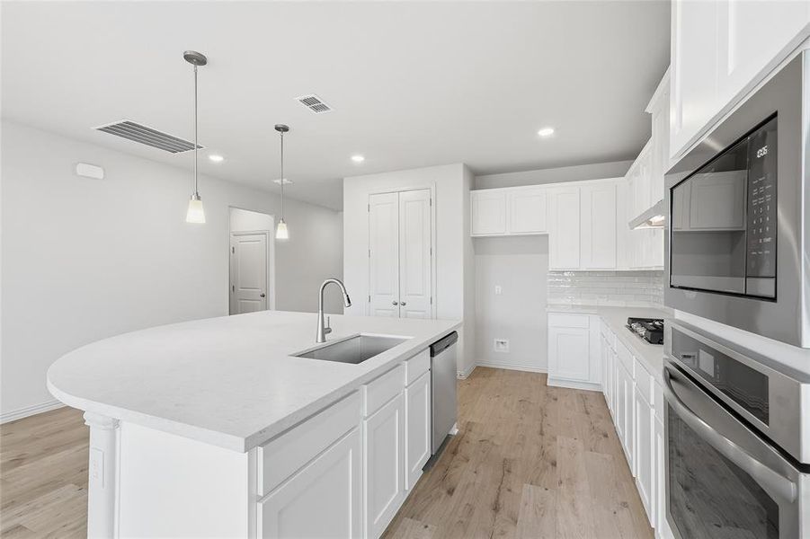 Kitchen with appliances with stainless steel finishes, white cabinets, pendant lighting, a kitchen island with sink, and light wood-style flooring Kitchen with appliances with stainless steel finishes, white cabinets, pendant lighting, a kitchen island with sink, and light wood-style flooring