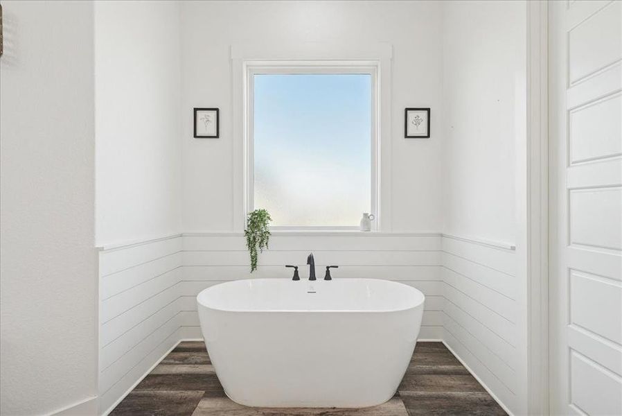 Bathroom featuring dark wood finished floors, a freestanding bath, and wainscoting