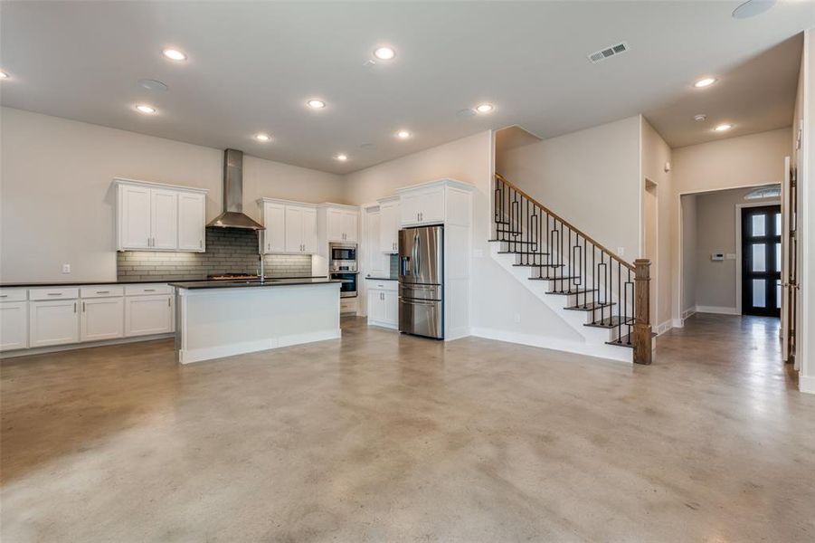 Kitchen featuring white cabinets, tasteful backsplash, an island with sink, appliances with stainless steel finishes, and wall chimney exhaust hood