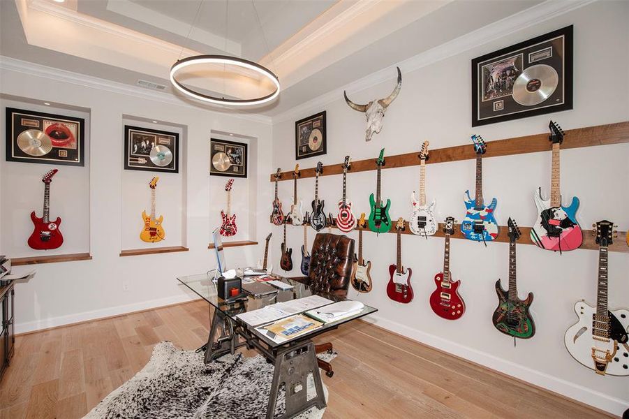 This room features a unique music-themed office with a collection of colorful guitars displayed on the walls. It includes framed records and awards, creating a creative and inspiring workspace. A modern glass desk and stylish lighting complete the look.